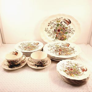 Może przedstawiać: Zestaw vintage porcelanowej zastawy stołowej z kwiatowym wzorem i ptakami. Zestaw zawiera dużą owalną paterę, talerze obiadowe, talerze sałatkowe, filiżanki do herbaty i spodki.
