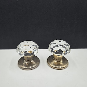 Peut inclure: Deux boutons de porte en cristal transparent avec des surfaces à facettes. Les boutons sont montés sur une base argentée avec une tige de couleur laiton. Le fond est noir et blanc.