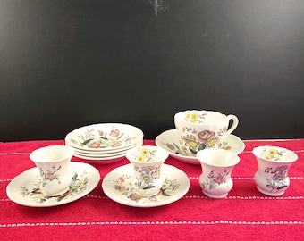Op de afbeelding: Een vintage set met bloemmotief theekopjes en schoteltjes. De kopjes en schoteltjes hebben een delicaat bloemmotief in roze, gele en groene tinten. De set bevat twee theekopjes, twee schoteltjes en twee kleine kopjes.