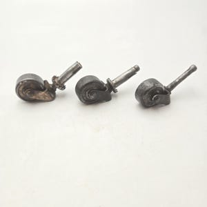 Peut inclure: Trois roulettes de meubles antiques en métal avec une finition sombre et vieillie. Chaque roue a une forme arrondie avec un axe central et une tige pour la fixation. Les roues sont probablement destinées aux meubles.