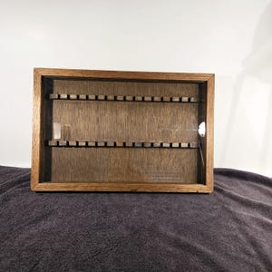 May include: A wooden display case with two shelves and a glass front. The case has 24 slots for displaying small items, such as coins or stamps.