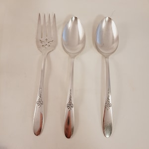 May include: Three silver-plated utensils: a fork with a decorative design and two spoons with floral patterns.