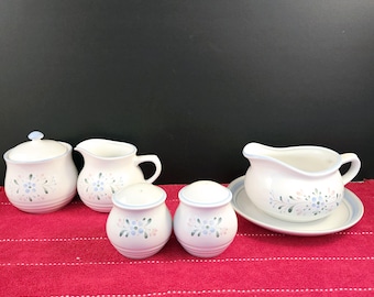 May include: A set of white ceramic kitchenware with a blue and pink floral design. The set includes a creamer, sugar bowl, gravy boat, and two salt and pepper shakers.