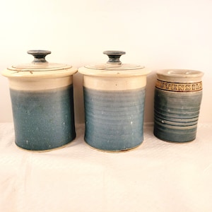 May include: Three ceramic kitchen canisters with blue and white glaze. The canisters have lids and are labelled "UTENSILS".