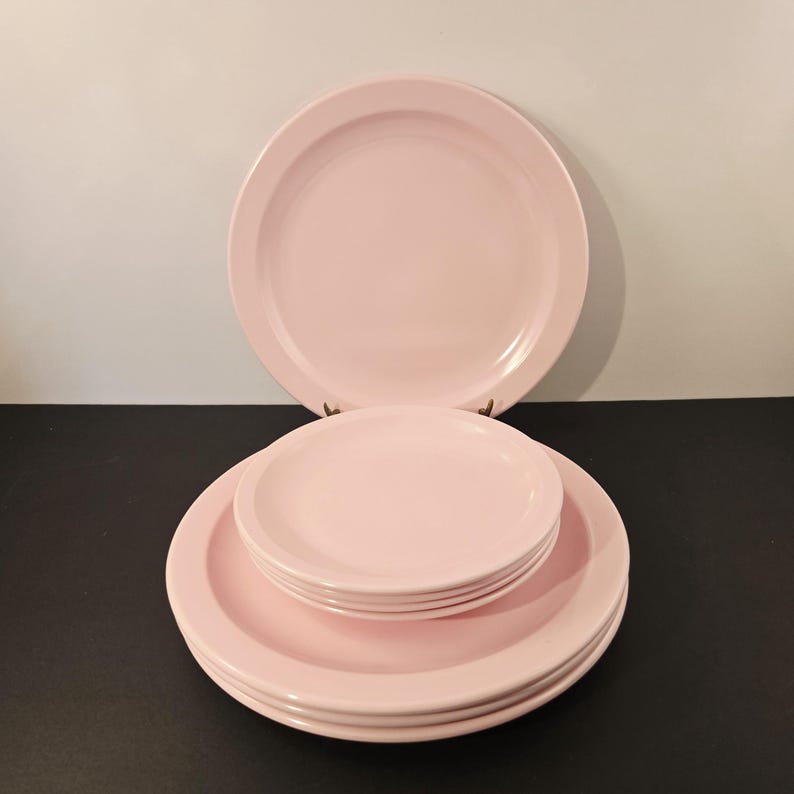 K&ouml;nnte beinhalten: Ein Satz rosa Keramikplatten in verschiedenen Gr&ouml;&szlig;en. Das Set umfasst gro&szlig;e Essteller und kleinere Teller, die &uuml;bereinander gestapelt sind. Die Teller haben ein schlichtes, klassisches Design und eine glatte, gl&auml;nzende Oberfl&auml;che.
