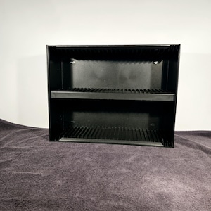 May include: Black metal shelf unit with two shelves and a slatted design. The shelf unit is empty.