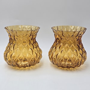 Op de afbeelding: Twee amberkleurige glazen vazen met een getextureerde, diamantpatroon buitenkant. De vazen hebben een uitlopende bovenkant en een afgeronde basis. Het glas heeft een warme, gouden tint en het ontwerp geeft ze een vintage uitstraling.