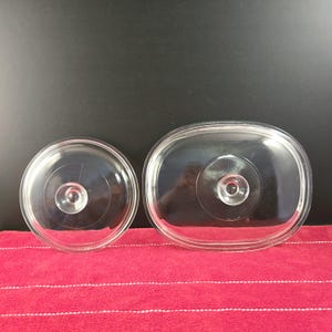 May include: Two clear glass lids for a casserole dish. The larger lid is oval shaped and the smaller lid is round.