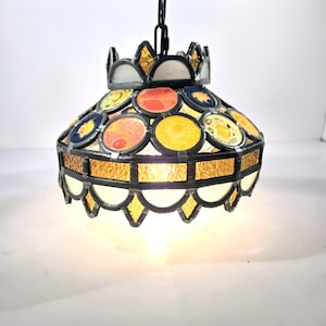 May include: A stained glass pendant light with a black chain. The lamp features a crown-like top and a shade with colourful circular glass pieces in shades of red, yellow, and blue. The bottom edge has a scalloped design.