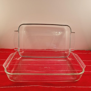 May include: Two clear glass baking dishes with handles. The dishes are nested together, with the smaller dish on top of the larger dish.