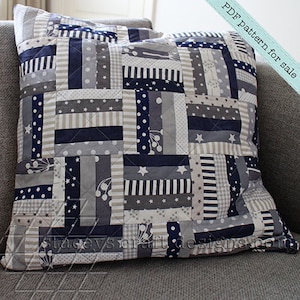 Op de afbeelding: Een patchwork kussenhoes met een geometrisch patroon in grijstinten, wit en marineblauw. De stof heeft verschillende patronen, waaronder strepen, stippen en sterren.