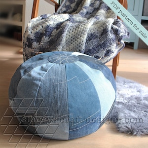 Op de afbeelding: Een ronde denim poef met een patchwork ontwerp. De poef is gemaakt van verschillende tinten blauw denim en heeft witte stiksels. De poef staat op een houten vloer.