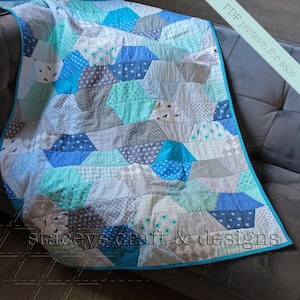 Op de afbeelding: Een PDF-patroon voor een quilt met een geometrisch ontwerp in tinten blauw, grijs en turquoise. De quilt is gemaakt van verschillende stoffen, waaronder sommige met kleine patronen. De quilt wordt getoond op een grijze bank. De tekst "PDF pattern for sale" en "staceys craft & designs" is zichtbaar in de afbeelding.
