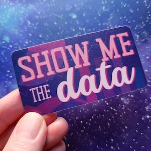 May include: A sticker with a purple, pink and blue geometric design. The sticker says "Show Me The Data" in pink letters.