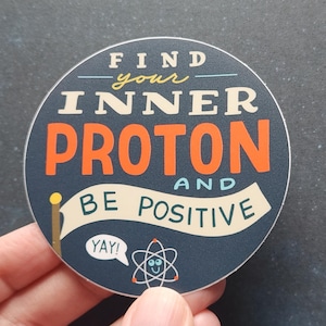 May include: A round sticker with the text "FIND your INNER PROTON AND BE POSITIVE" in white, orange, and blue. A small atom graphic and the word "YAY!" are also included. The sticker has a dark blue background.