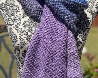 May include: A purple and blue ombre scarf with a sparkly finish. The scarf is crocheted and is displayed on a mannequin.