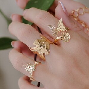 Puede incluir: Un conjunto de cuatro anillos dorados con diseños inspirados en la naturaleza. Los anillos incluyen una mariposa, una flor, una hoja y un corazón con una vid.