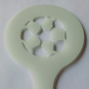Puede incluir: Una plantilla de plástico blanco con forma de balón de fútbol con un agujero en el centro. La plantilla tiene un mango.