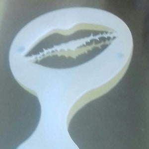 Puede incluir: Plantilla de plástico blanco en forma de labios con un diseño detallado. La plantilla está diseñada para crear arte de latte.