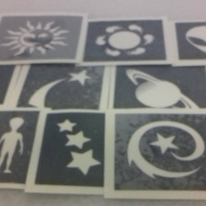 May include: A set of 12 space-themed stencils, featuring designs such as a UFO, a rocket ship, a crescent moon, a shooting star, a planet with rings, and a sun. The stencils are made from a thin, flexible material and are ideal for creating unique designs on various surfaces.