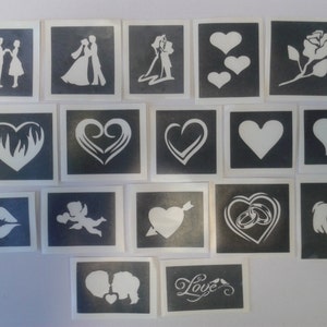 May include: A set of 16 black and white stencils featuring various wedding-themed designs, including hearts, rings, a couple, a rose, and the word "Love".