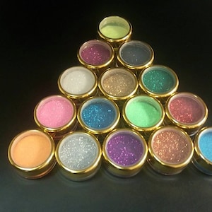 Peut inclure: Un arrangement triangulaire de 15 petits contenants ronds remplis de paillettes de différentes couleurs. Les contenants ont des couvercles dorés et des côtés en verre transparent.