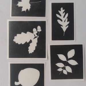 May include: Five black and white stencils with various leaf and acorn designs. The stencils are on a white background.