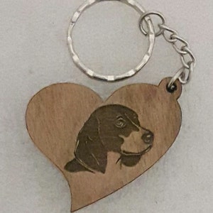 May include: Wooden heart-shaped keyring with a laser-engraved image of a beagle dog's head. The keyring has a silver metal ring and chain.