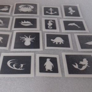 Puede incluir: Un conjunto de 16 plantillas en blanco y negro con varias criaturas marinas, incluyendo una ballena, un cangrejo, un ancla, una sirena, un delfín, una estrella de mar, un caballito de mar, una tortuga, un pulpo, una foca, un tiburón, un surfista, un pingüino y una sirena con cola.