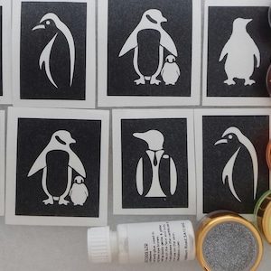 Puede incluir: Un conjunto de ocho plantillas de pingüinos con un frasco de pegamento y seis frascos de purpurina de varios colores. Las plantillas son negras con diseños de pingüinos blancos. La purpurina es plateada, roja, naranja, verde y amarilla.