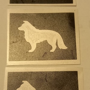 May include: Three white silhouette stencils of a dog on a dark grey background. The dog is standing with its tail curled.