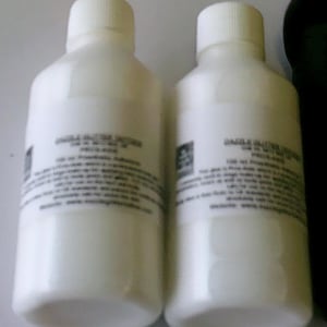 Puede incluir: Dos botellas de plástico blancas con etiquetas que dicen "Solución para gargarismos/Antiséptico" y "100 ml/3,38 fl oz".