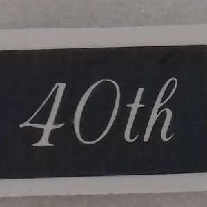Könnte beinhalten: Eine schwarze Plakette mit einer weißen Aufschrift, die "40th" lautet.