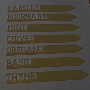 May include: Seven brown plant markers with white lettering. The markers are labelled: Parsley, Rosemary, Mint, Chives, Oregano, Basil, and Thyme.