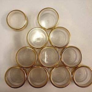 May include: A group of ten clear glass jars with gold lids. The jars are arranged in a pyramid shape.