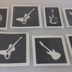 Op de afbeelding: Acht zwart-witte gitaar sjablonen op wit karton. De sjablonen tonen verschillende gitaarontwerpen, waaronder een gitaar met vlammen, een gitaar met een gat in de body en een standaard elektrische gitaar.