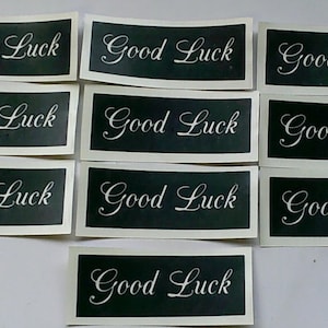 Puede incluir: Nueve pegatinas blancas con fondo negro y el texto "Good Luck" escrito en letra cursiva blanca.