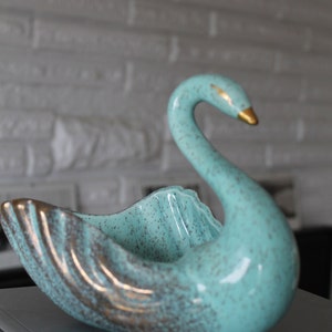 May include: A teal blue ceramic swan figurine with gold accents. The swan has a speckled finish and is shaped like a bowl.