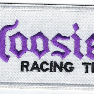 Puede incluir: Parche rectangular blanco con texto bordado en morado "Hoosier Racing Tire" en una fuente gótica.
