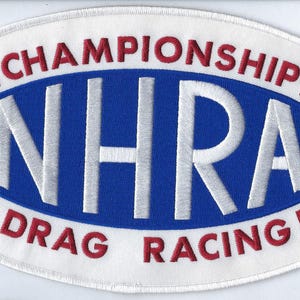May include: An oval-shaped embroidered patch featuring the NHRA logo in white lettering on a blue background. The text CHAMPIONSHIP is arched above and DRAG RACING is arched below in red, all bordered by a white edge with a registered trademark symbol.