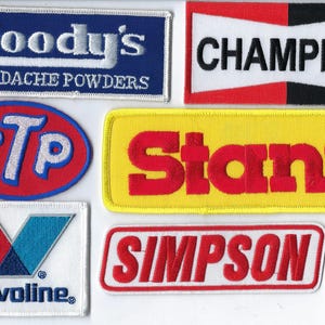 May include: A collection of six embroidered patches featuring various brand logos. The patches include Goody's Headache Powders, Champion, STP, Stant, Valvoline, and Simpson. Each patch displays distinct colors, including blue, red, yellow, white, and black.