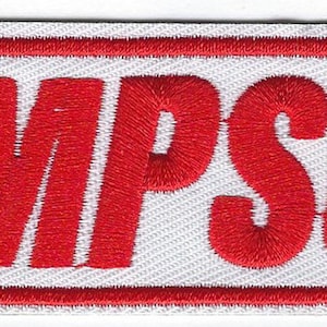 May include: Embroidered patch with the name "SIMPSON" in bold red letters. The text is stitched onto a white background, framed by a red border. The patch has a rectangular shape.