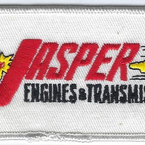 May include: A rectangular white embroidered patch featuring the red text JASPER and black text ENGINES & TRANSMISSIONS. It includes a green cartoon figure, a yellow starburst, a yellow engine icon, and a green map shape with the text GO!.