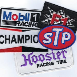 May include: A collection of embroidered racing patches. The patches feature logos for Mobil 1 Racing, Champion, STP, and Hoosier Racing Tire. The patches are in various shapes and colors, including red, white, blue, and black.