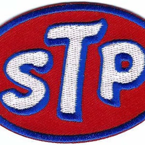 May include: Embroidered STP patch with a red oval background and a blue border. The letters "STP" are in white with blue outlines. This patch is likely for automotive or racing enthusiasts.