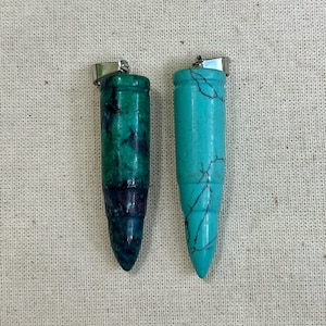 May include: Two bullet-shaped pendants, one green and one blue, with silver metal accents. The pendants are made of stone and have a smooth, polished finish.