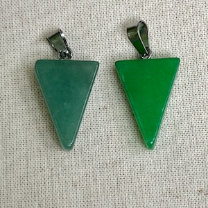 May include: Two green triangle-shaped pendants with silver bail loops. The pendants are made of polished stone.