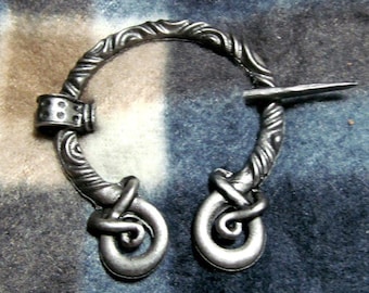 May include: A silver metal brooch with a circular design and two decorative loops. The brooch has a pin that is attached to the circle.