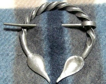 May include: A silver metal ring brooch with a twisted wire design and two pointed ends. The brooch is on a blue and white patterned fabric.