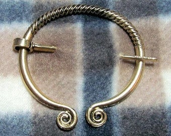 May include: A gold-toned metal Celtic knot brooch with a twisted wire design and a circular shape. The brooch has a pin and catch closure.